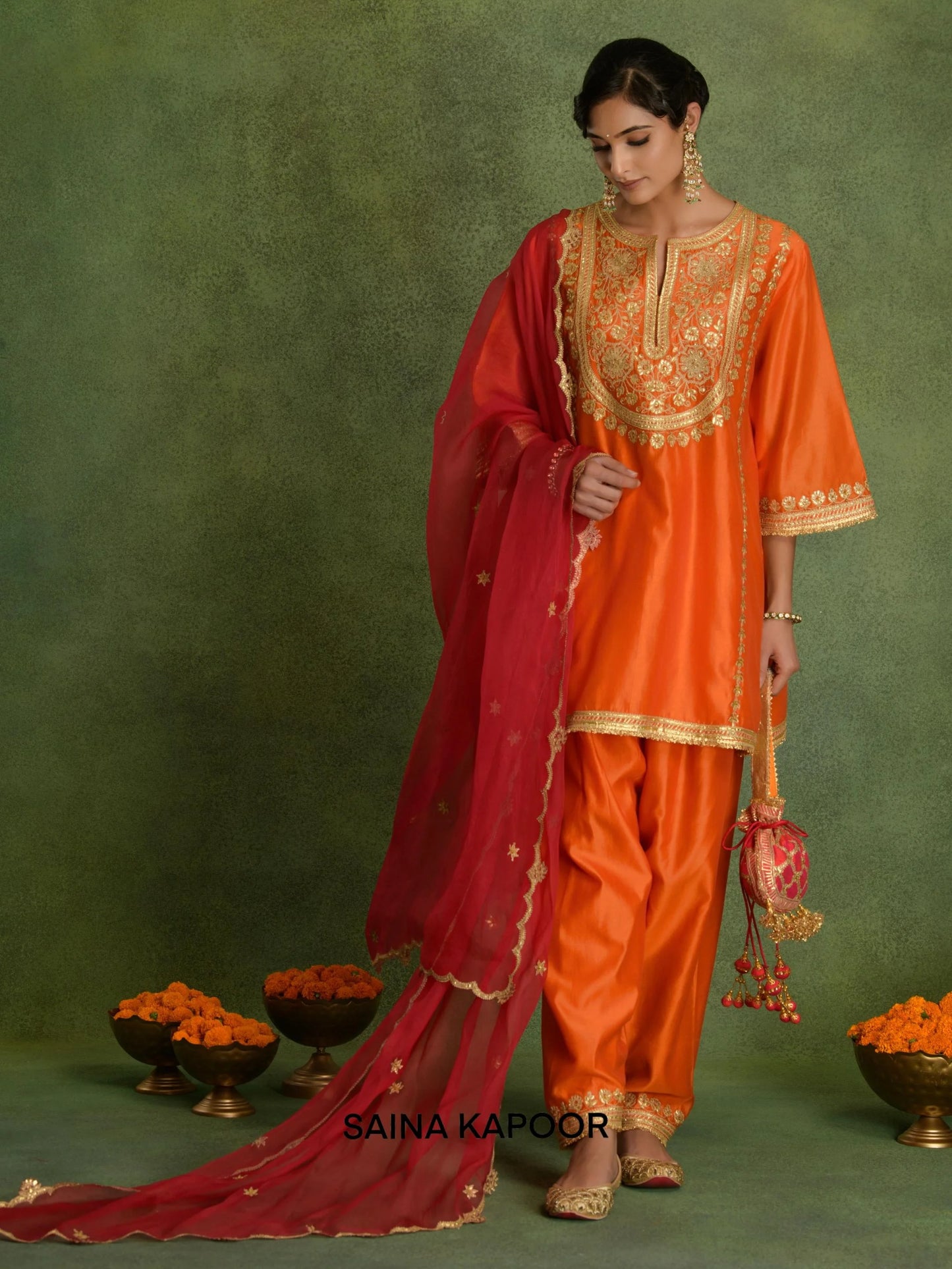 Deep orange Chanderi short kurta DARSHITA with gold gota patti floral embroidered V-notch yoke, matching dhoti salwar with embroidered ankle cuffs, contrasting red dupatta & pink potli bag — Saina Kapoor