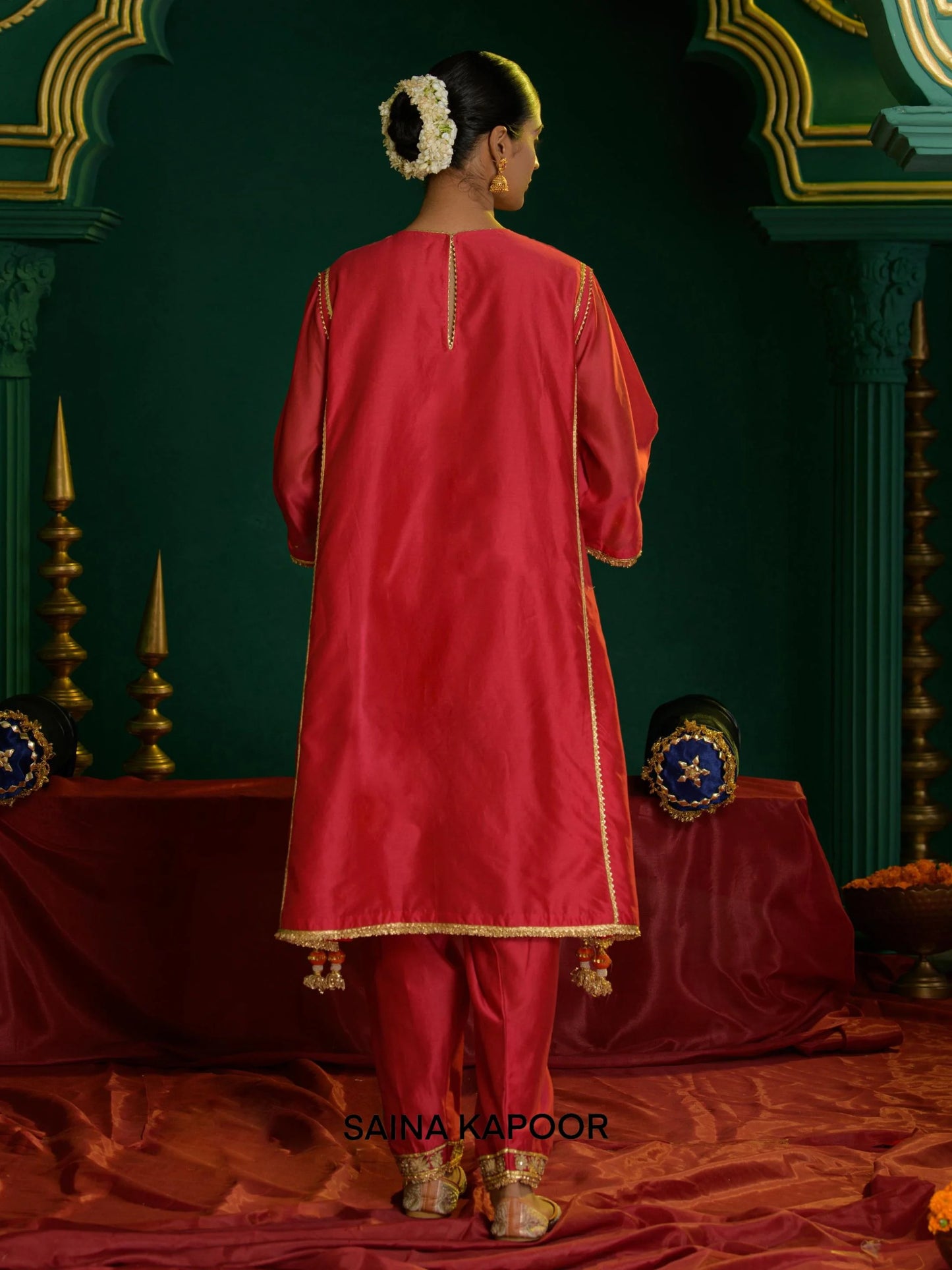 Back view of coral red Chanderi long choga set for women showing open-front gold gota border, three-quarter sleeve cuffs & matching dhoti salwar with embroidered ankle cuffs — Saina Kapoor