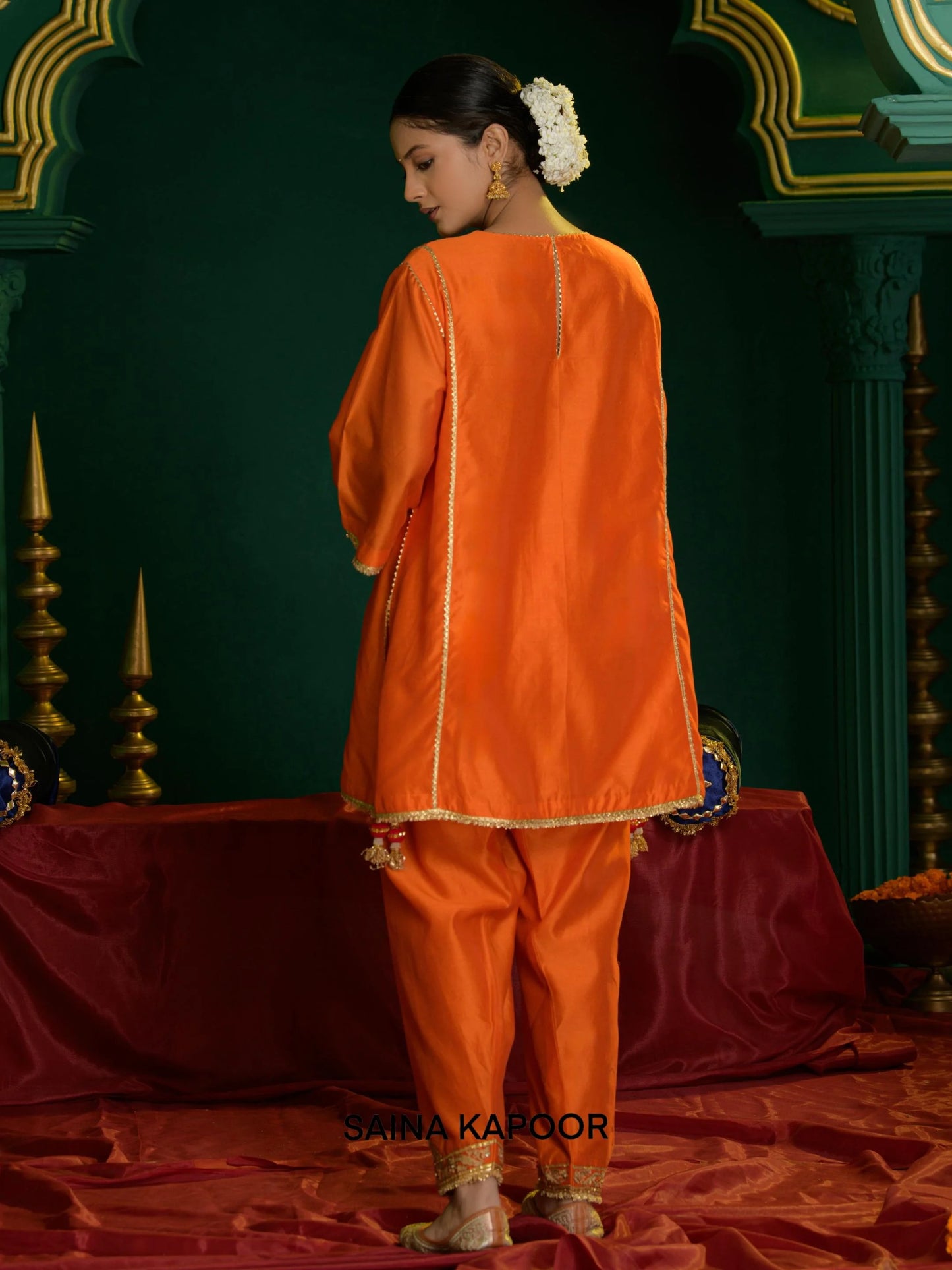 Back view of deep orange Chanderi short choga set for women showing open-front gold gota border, three-quarter sleeve cuffs & matching dhoti salwar with embroidered ankle cuffs — Saina Kapoor