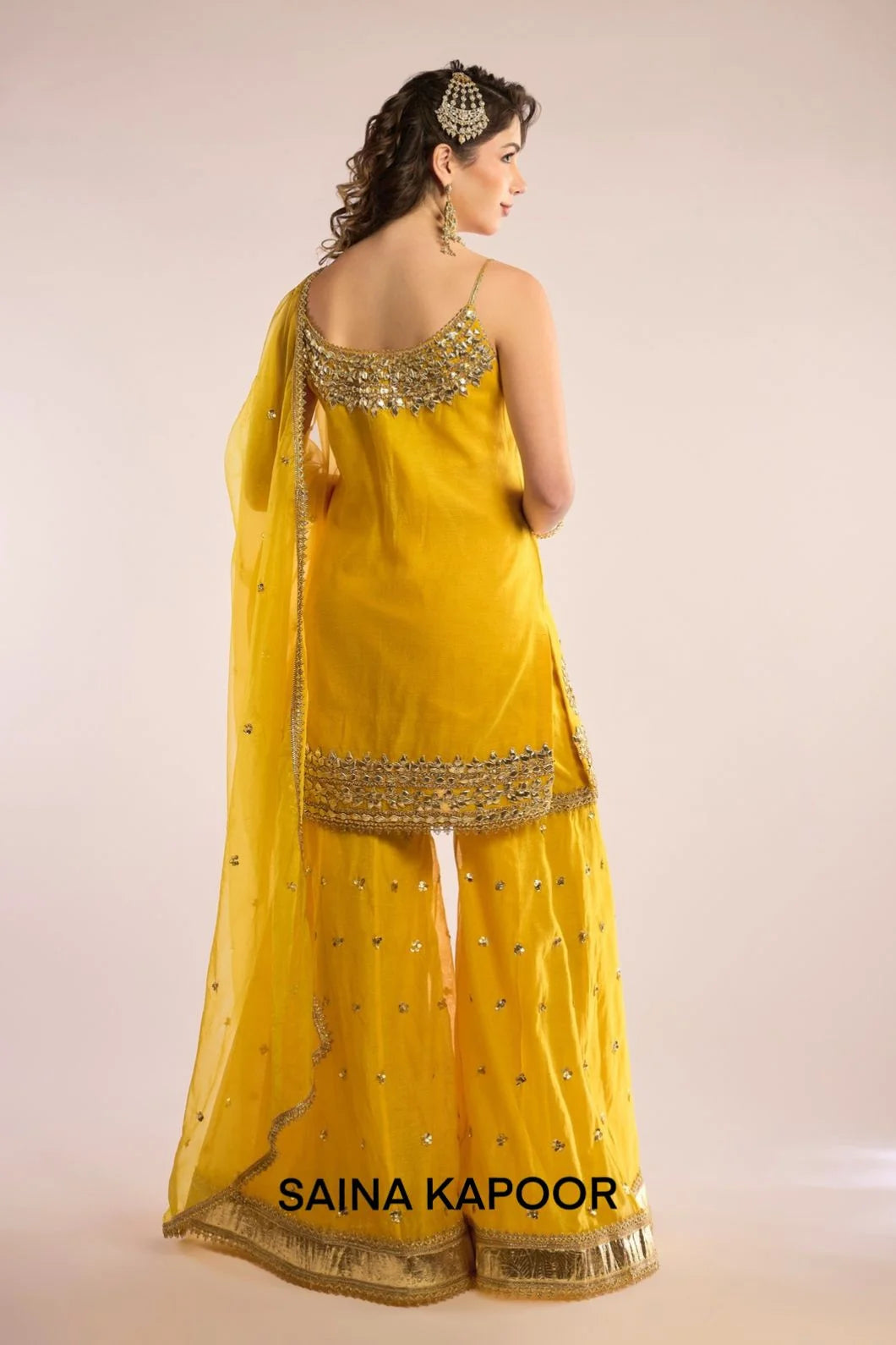 Back view of yellow Chanderi kurti gharara set for women with draped yellow organza dupatta — Saina Kapoor