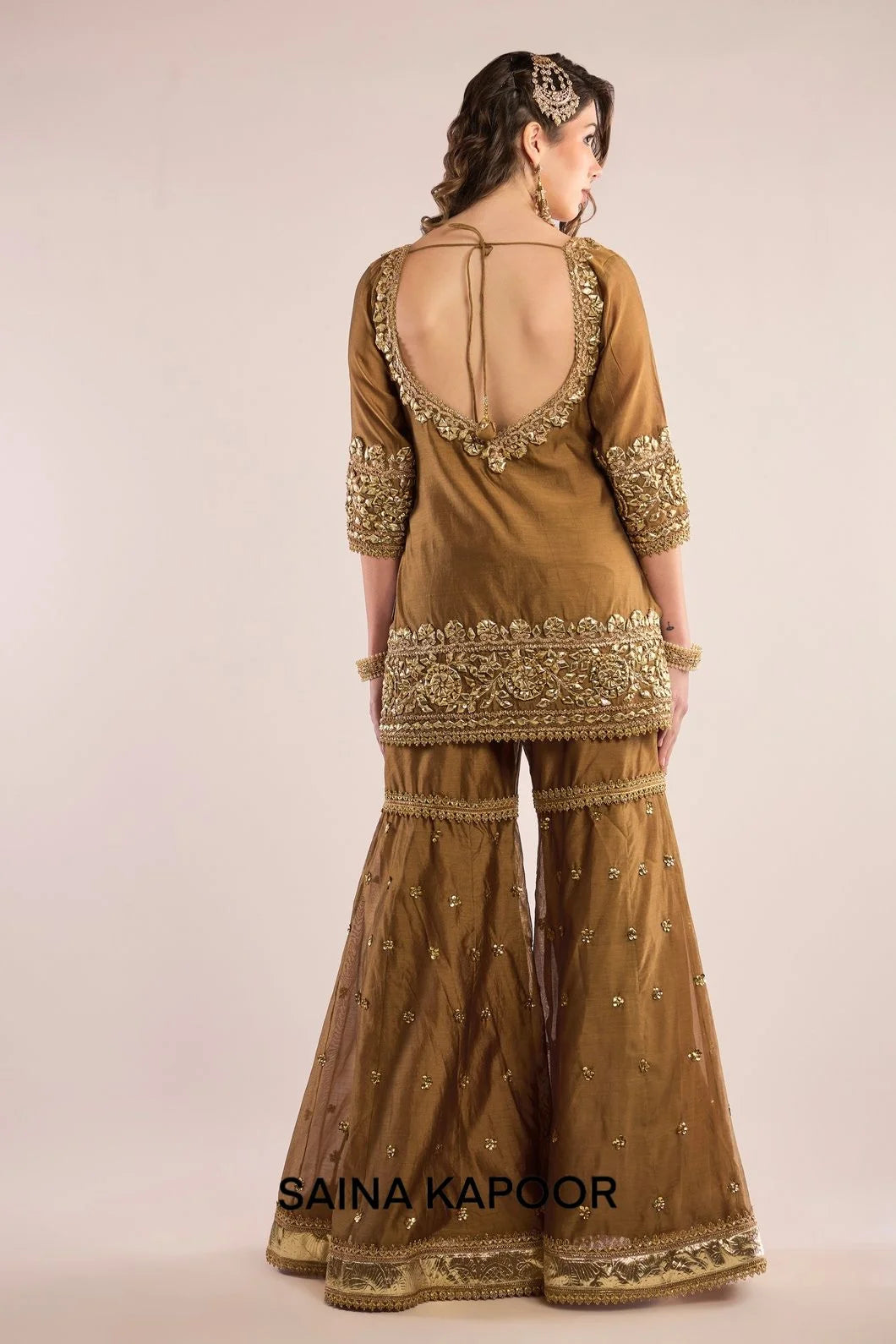 Back view of gold Chanderi kurta gharara set for women with draped champagne organza dupatta — Saina Kapoor
