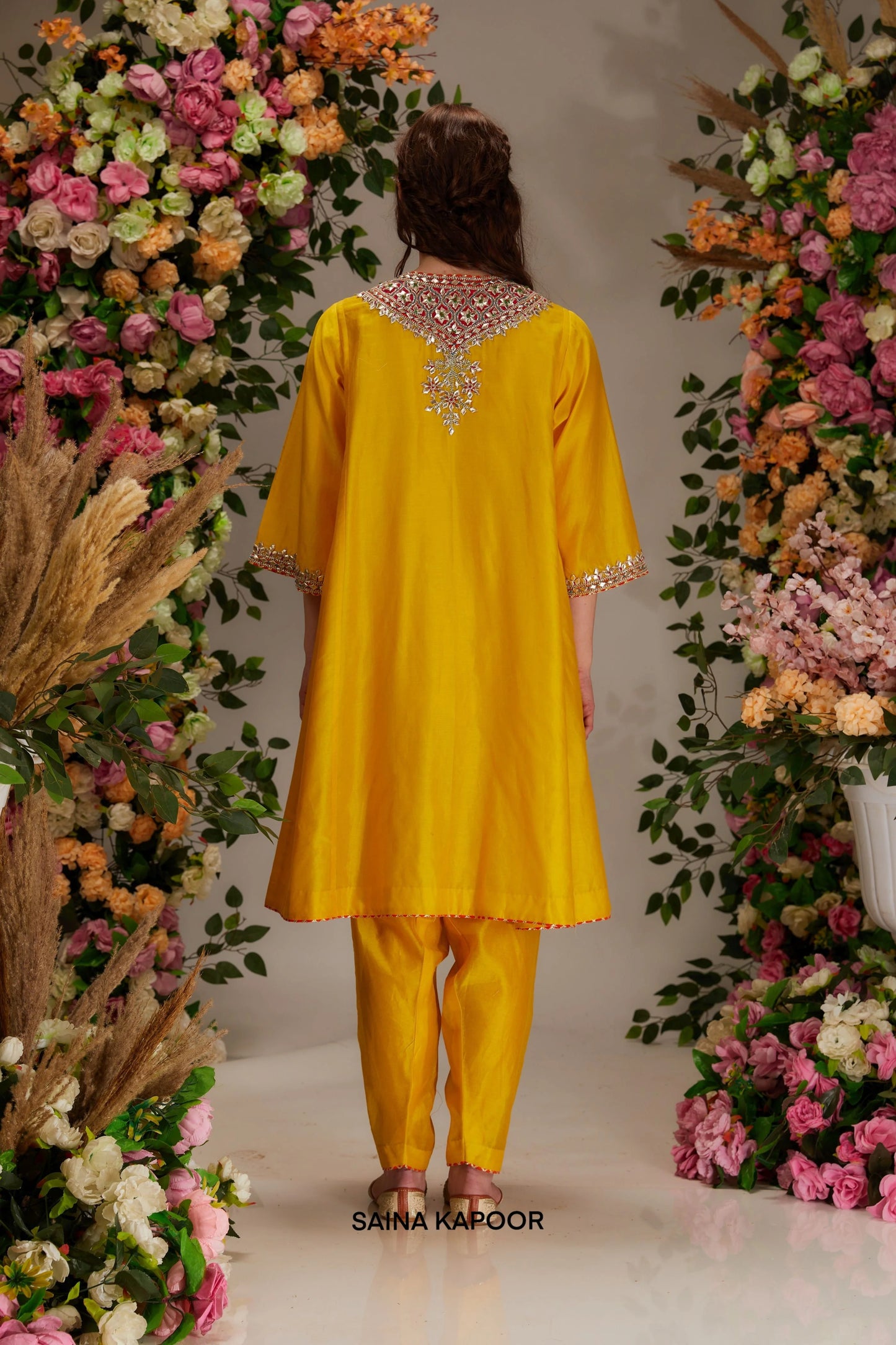Back view of yellow Chanderi short kalidar kurta set for women with draped orange organza dupatta — Saina Kapoor